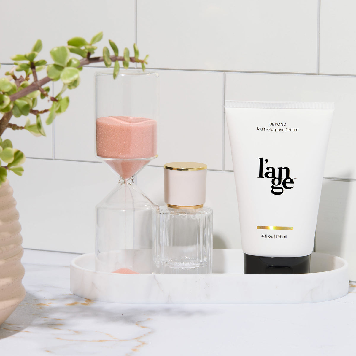 L’ange Beyond Multi-Purpose Cream displayed on a vanity tray with an hourglass, a small bottle, and a potted plant.