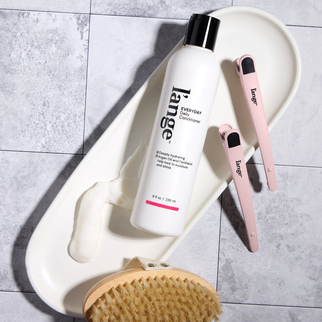 Overhead view of L’ange Conditioner with a body brush and clips on a grey tile surface