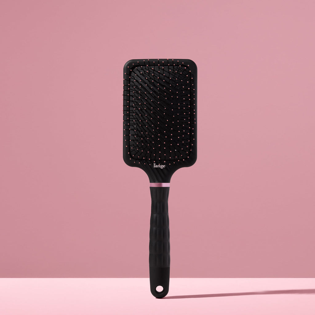 black L’ange detangling paddle brush with nylon bristles standing upright on pink background