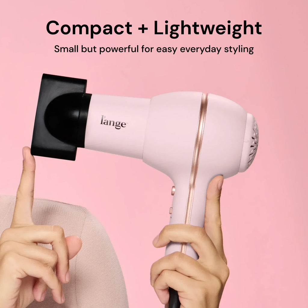 Hands holding L'ange Hot Stuff blush hair dryer with concentrator on pink background. "Compact + Lightweight – Small but powerful for easy everyday styling"
