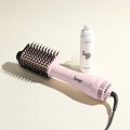 The Effortless Blowout Duo Value Set, featuring a Blush Le Volume Eleve brush and Glass Hair spray, displayed against a beige background