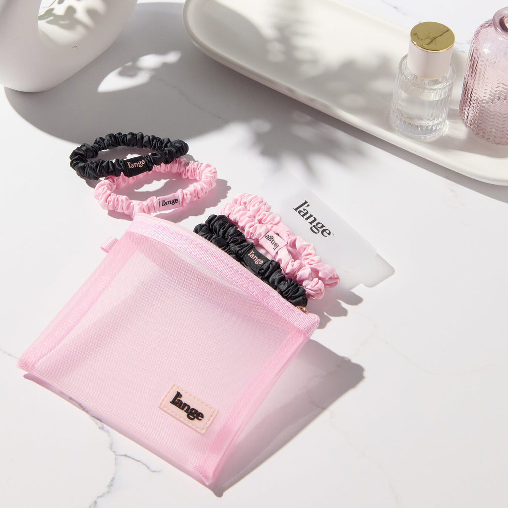 blush and black L’ange satin scrunchies on a vanity beside a small pink zip pouch