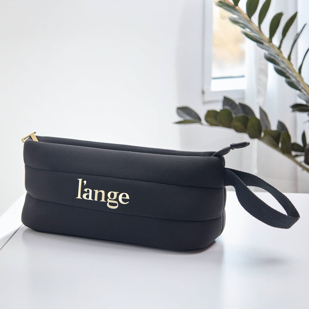Black L’ange zippered cosmetic bag with gold logo and wrist strap on a white surface.