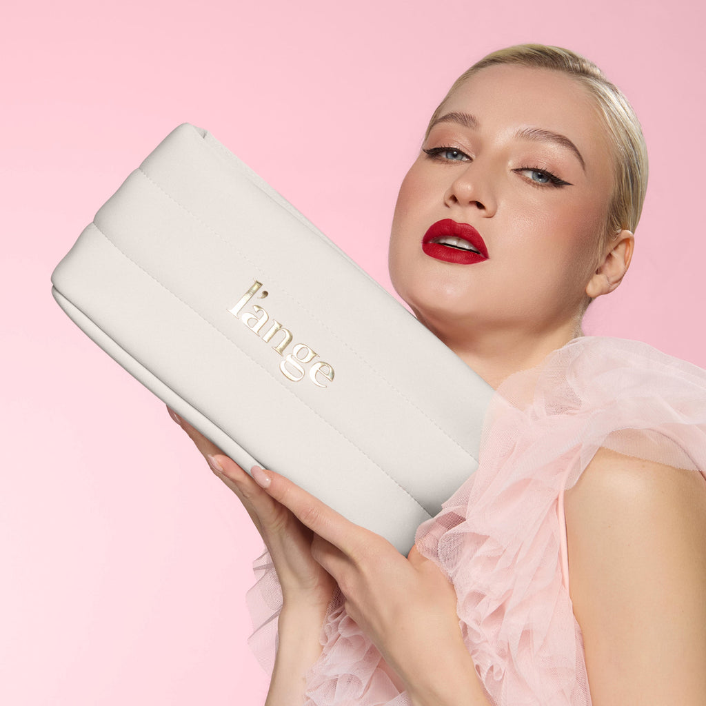 Model holding white a L’ange bag against pink backdrop