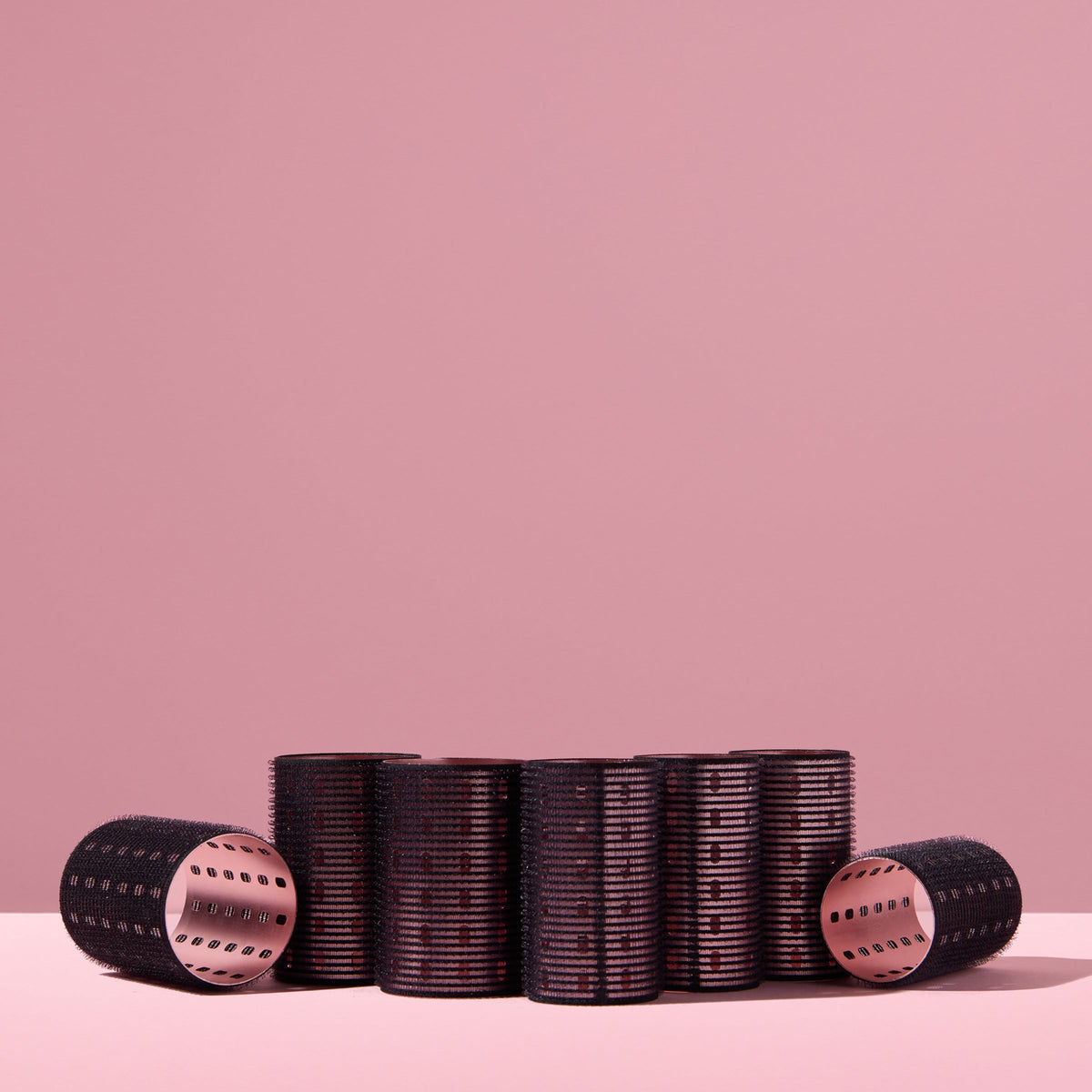 A collection of black thermal hair rollers, arranged on a pink background
