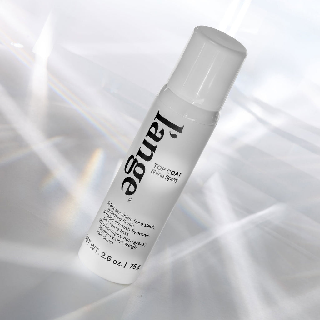 L'ange Top Coat Shine Spray bottle angled on a reflective surface with light prism effects.