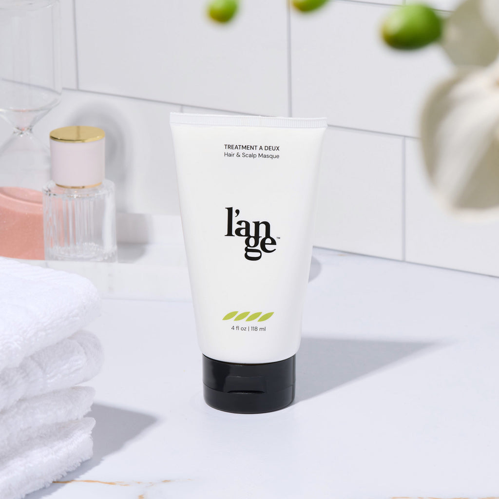L’ange Treatment à Deux Hair & Scalp Masque displayed on a bathroom counter with towels and decor.