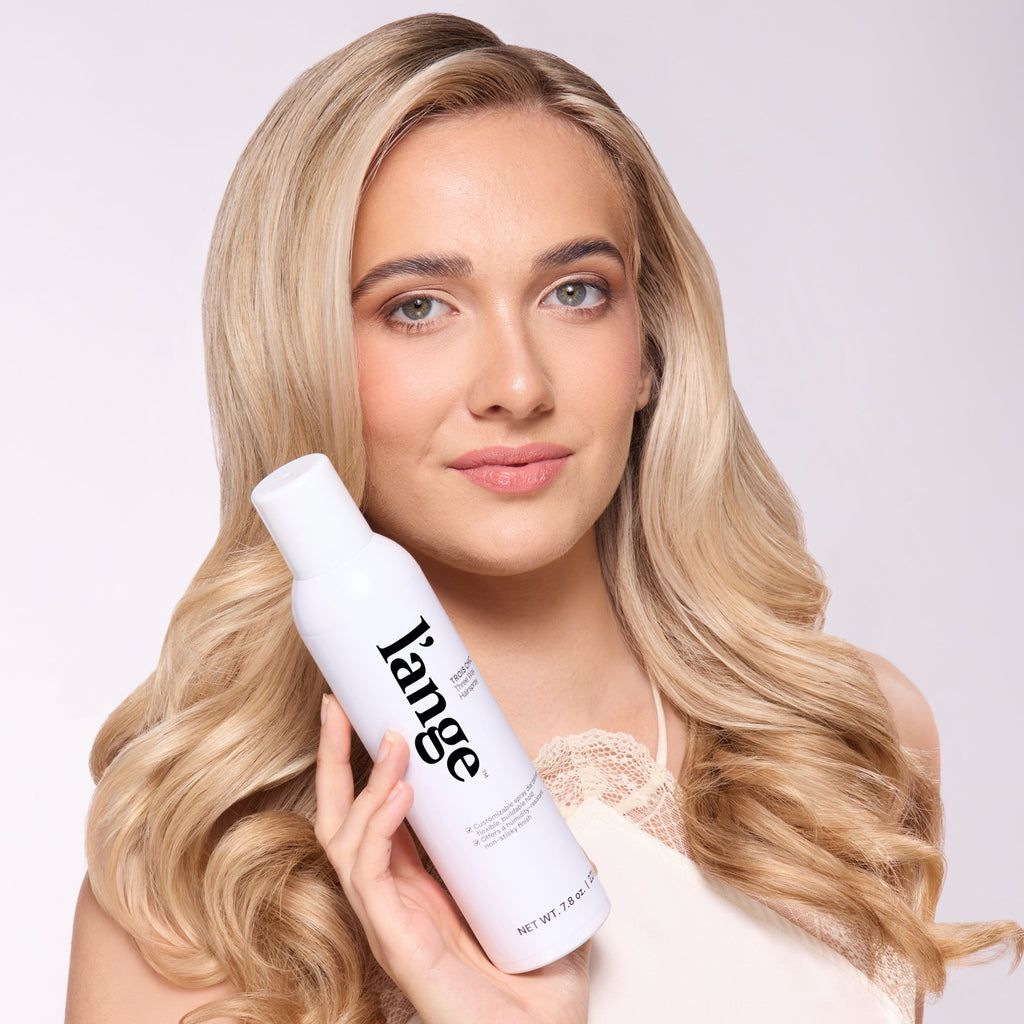 Woman with long, loose waves holding L’ange Trois Chic Three Way Hairspray bottle