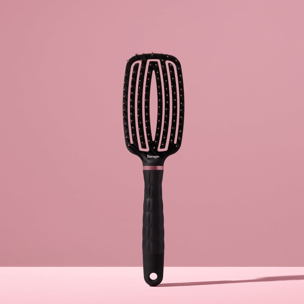 black L’ange vented paddle brush with nylon bristles standing upright on pink background