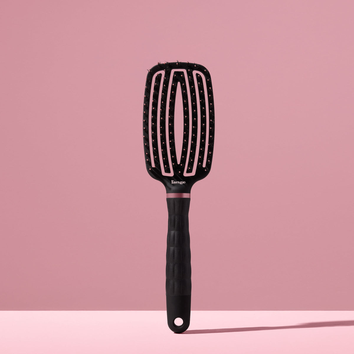 black L’ange vented paddle brush with nylon bristles standing upright on pink background